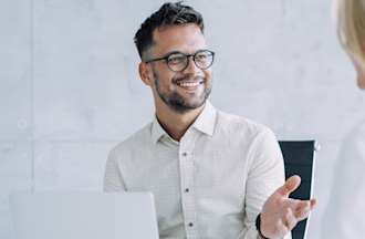 [Featured image] A Java developer sits at his desk with a laptop and talks about his next project with a colleague. 
