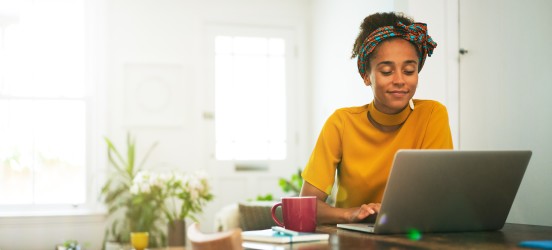 [Featured Image] A woman works on a laptop at a living room table.