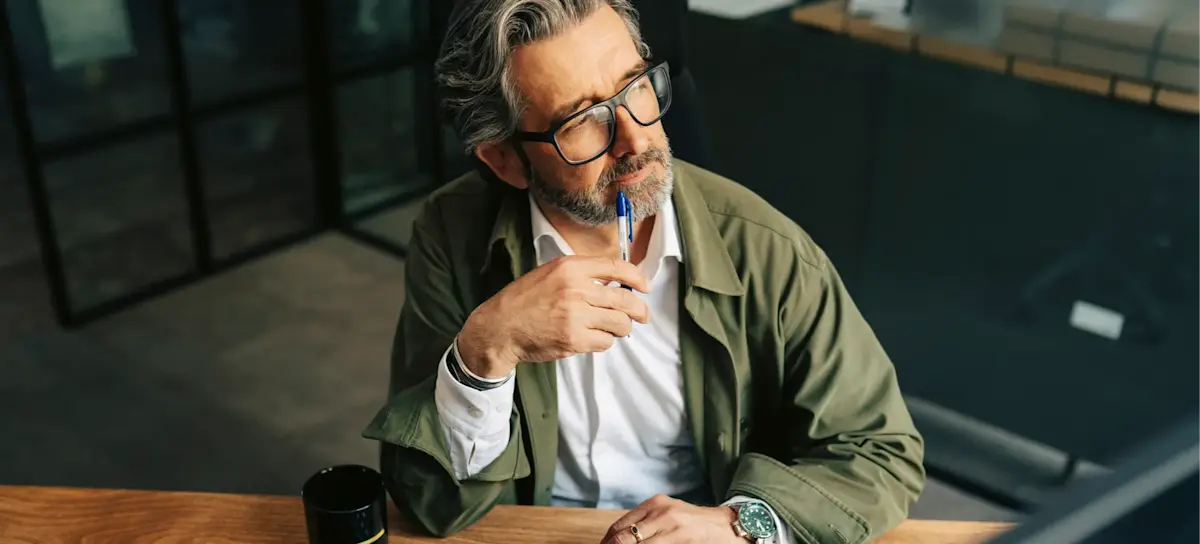 [Featured Image] An entrepreneur sits at their computer, pensively looking out a window after learning how to use ChatGPT to start a business and beginning to brainstorm business ideas.