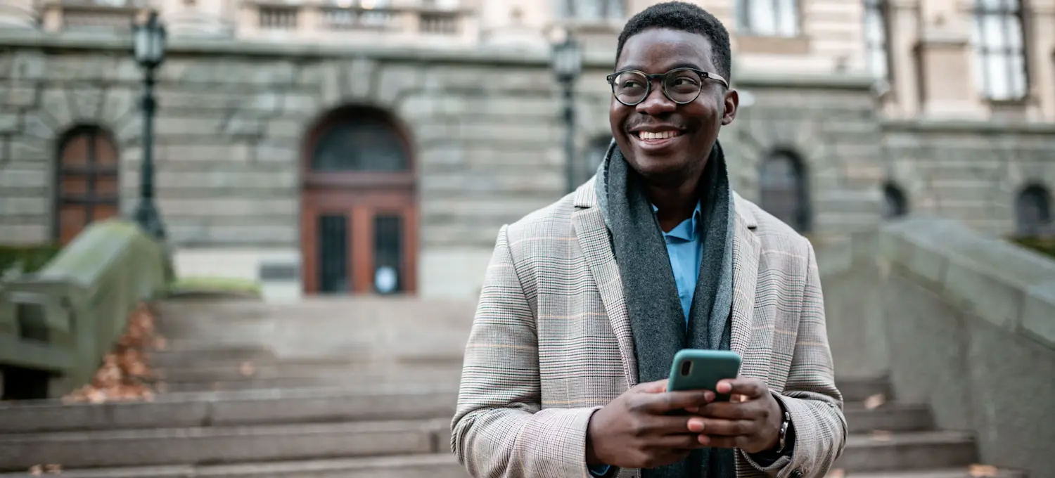 [Featured image] An aspiring business school student checks their GMAT score on their phone outside a university building.