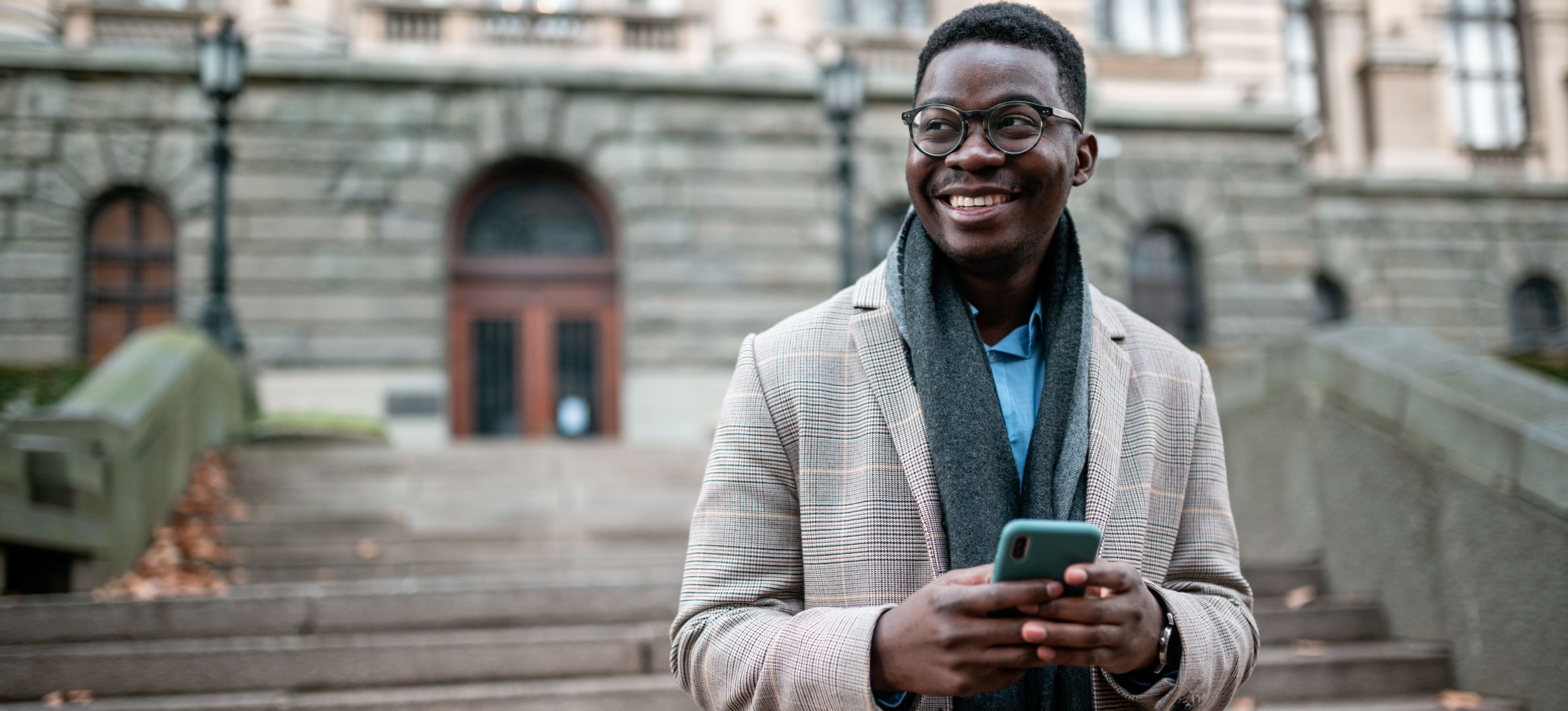 [Featured image] An aspiring business school student checks his GMAT score on their phone outside a university building.