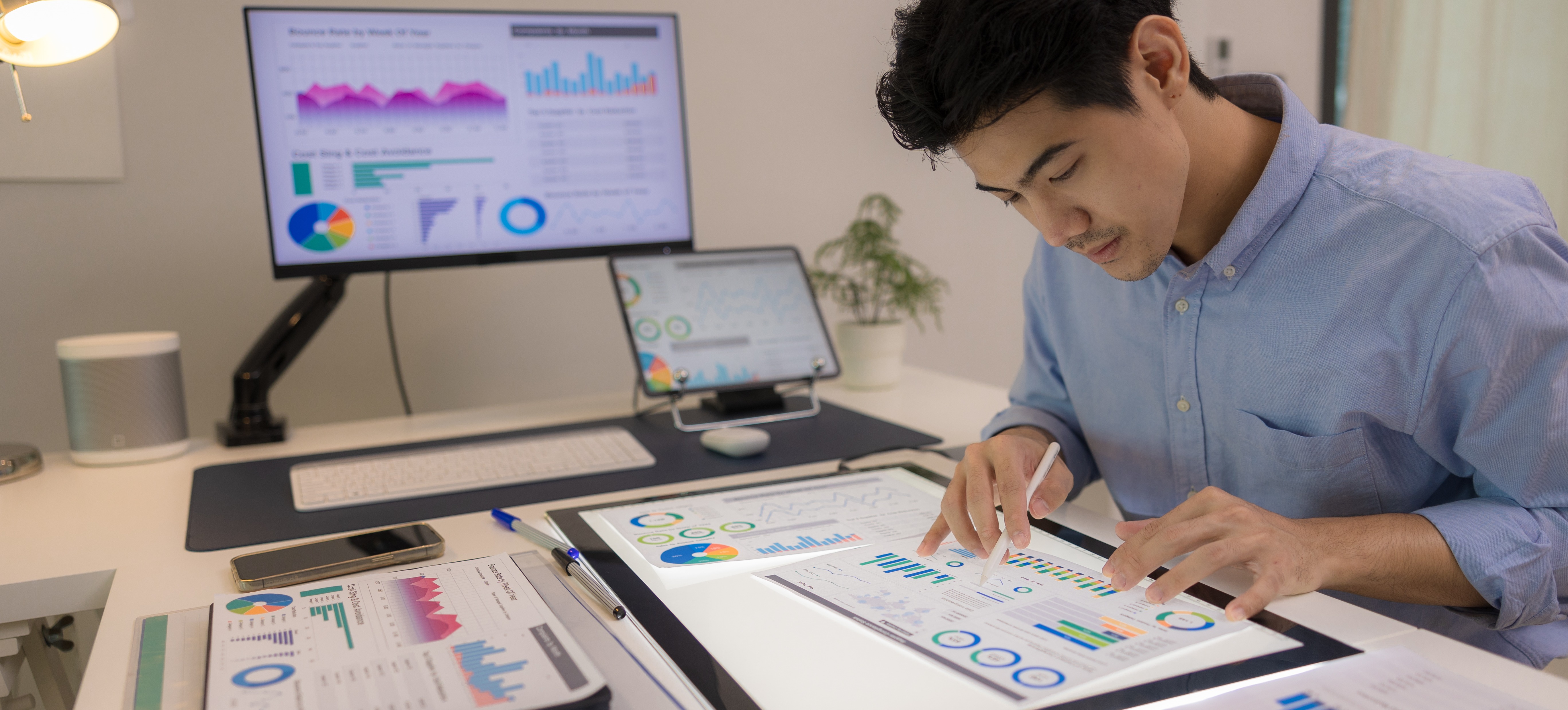 [Featured Image] A data analyst looks at graphs while a dashboard is displayed on a computer monitor in the background.
