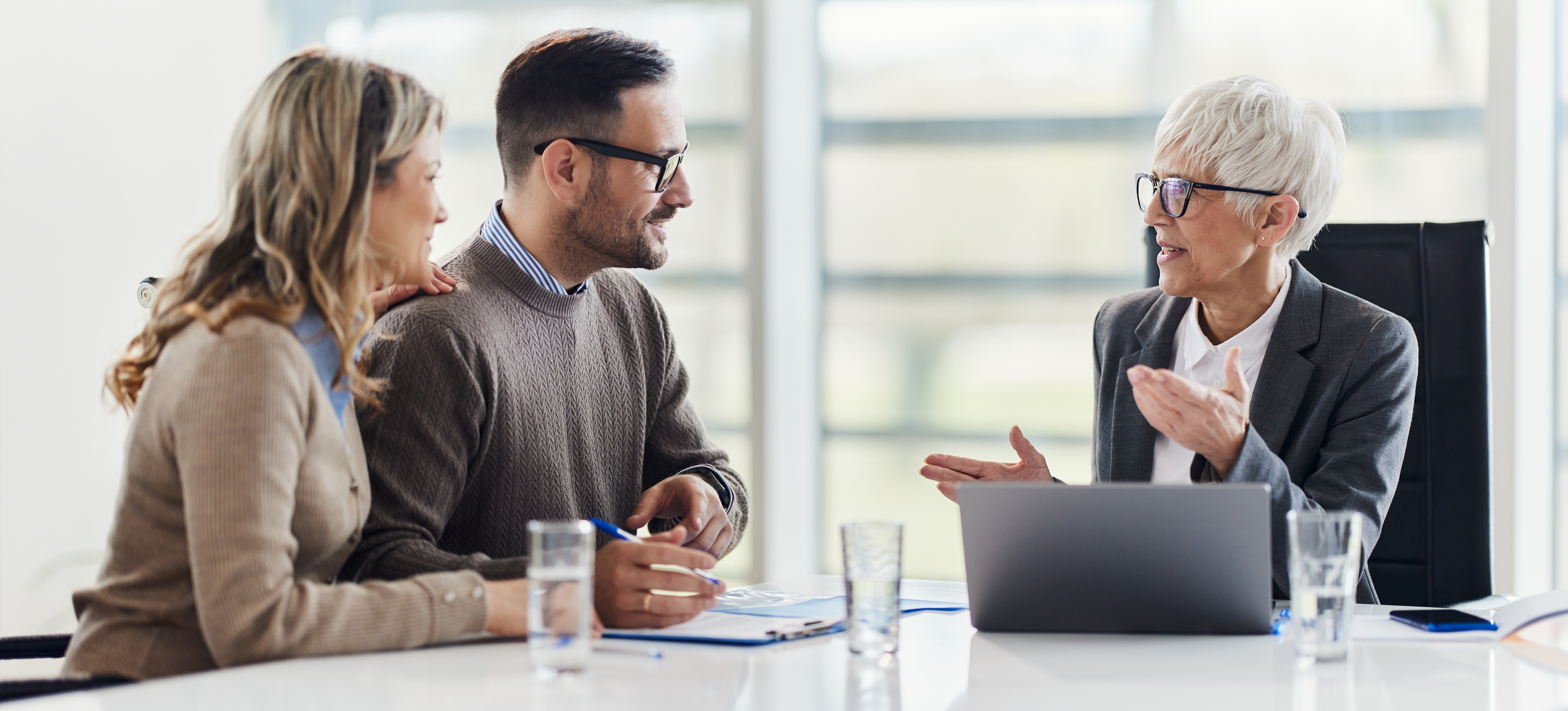 [Featured Image] A person earning a tax advisor salary meets with two clients in their office to discuss what they will pay in taxes this year.
