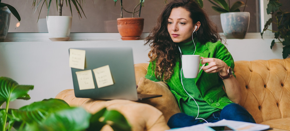 [Featured image] An email marketing manager and sweater sits on an orange sofa and works on their laptop.
