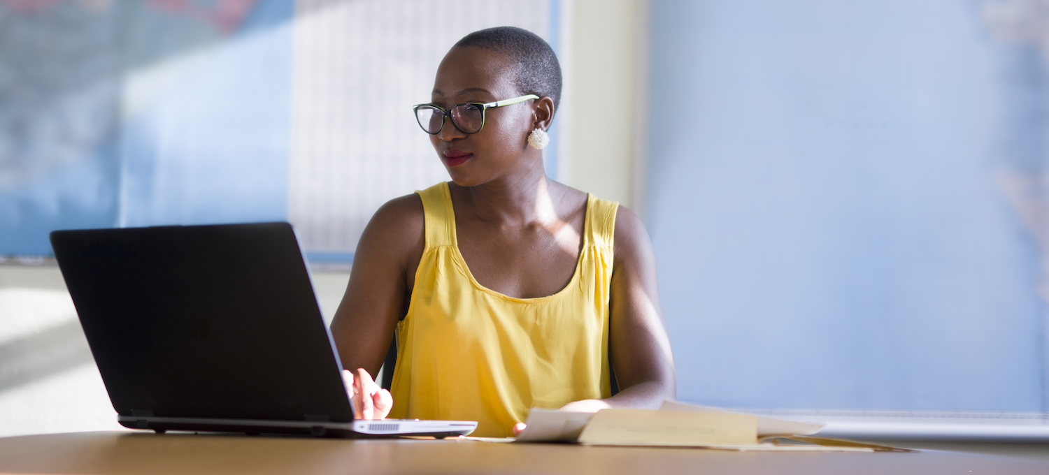[Featured image] A data analyst wearing a yellow tank top and eyeglasses sits in front of a laptop in an office analyzing Python vs. R.