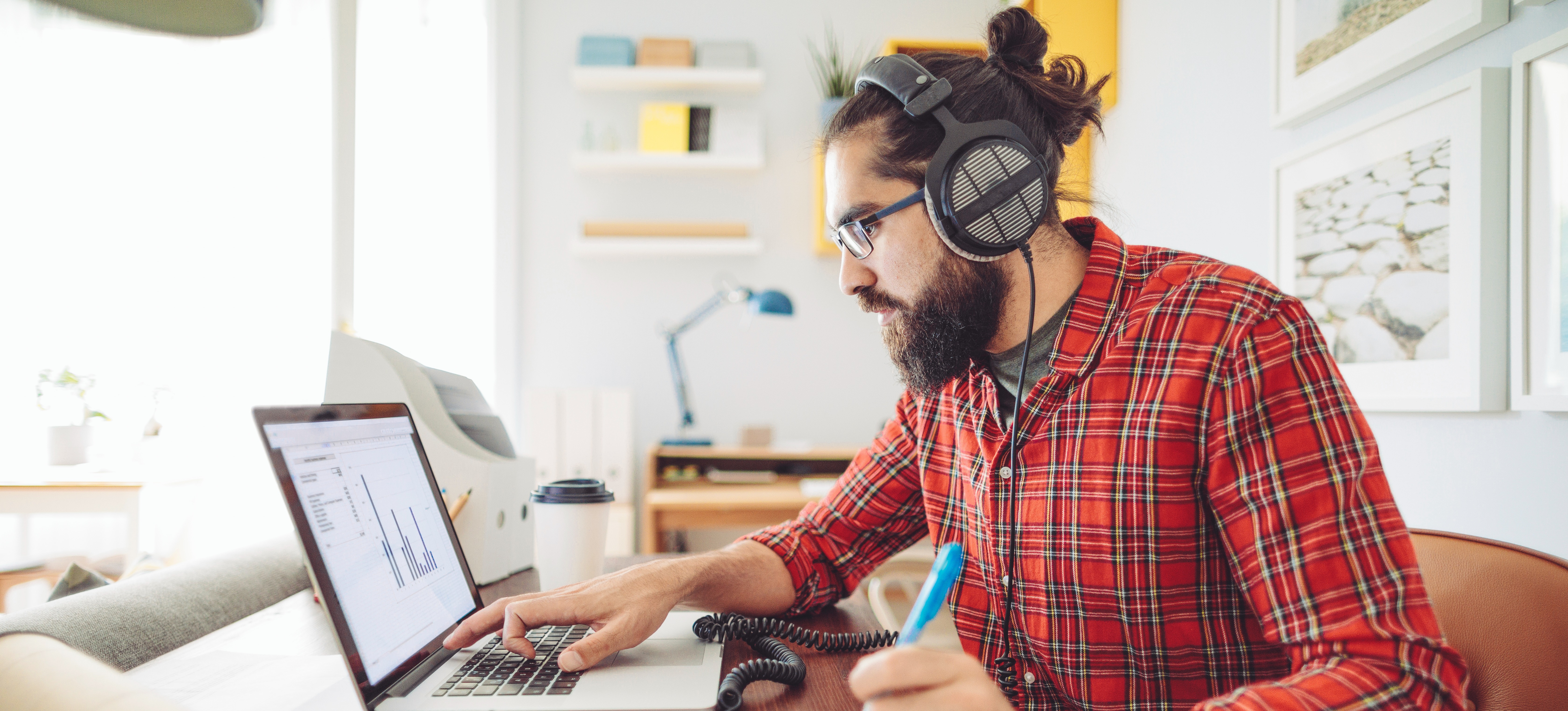 [Featured Image] A man wearing headphones sits at a desk and works on his IoT project. 