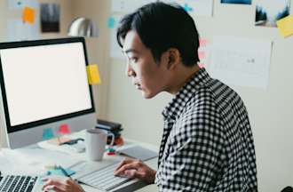 [Featured Image] A man in a checkered shirt searches programming languages to learn on his computer. 