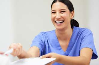 [Featured Image] A young dark-haired physician assistant, working in one of the jobs in demand in Florida, smiles and hands a pen and paperwork to a dark-haired patient.
