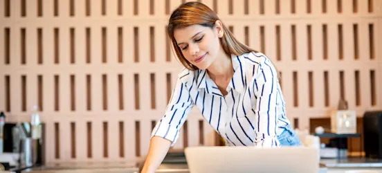 [Featured Image] A finance project manager makes some notes about a project on a pad of paper at their desk. 
