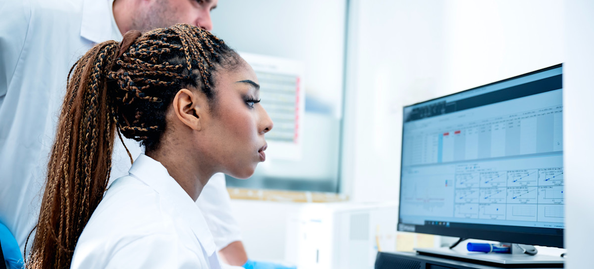 [Featured Image] Two medical professionals review AI-powered transcription notes recently added to a patient’s medical record, which is one of many uses for AI in medicine. 
