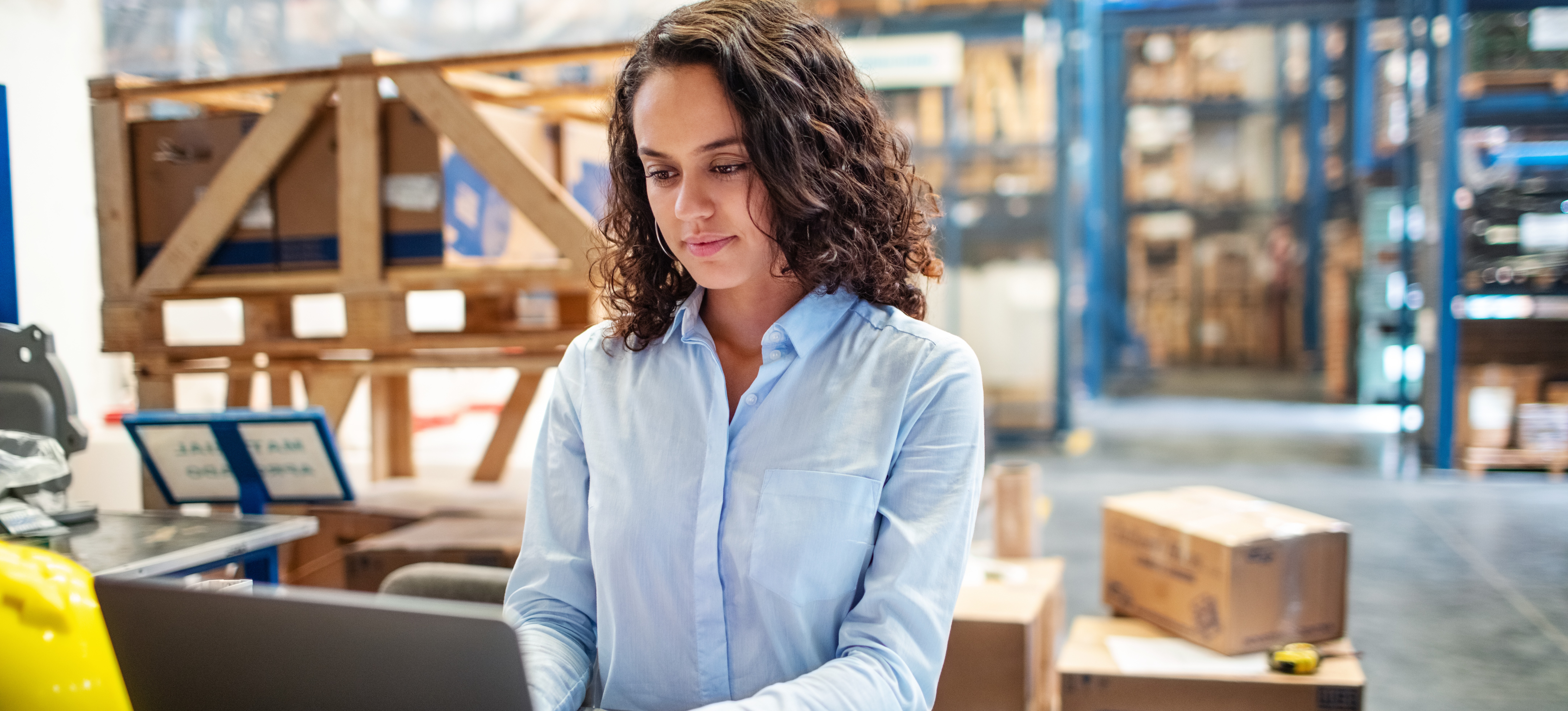 [Featured image] A businessperson sits at a laptop in a warehouse and uses the SCOR model to improve their organization's supply chain management decisions. 
