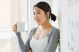 [Featured Image] A woman is leaning against a whiteboard with a coffee mug in her hand. 