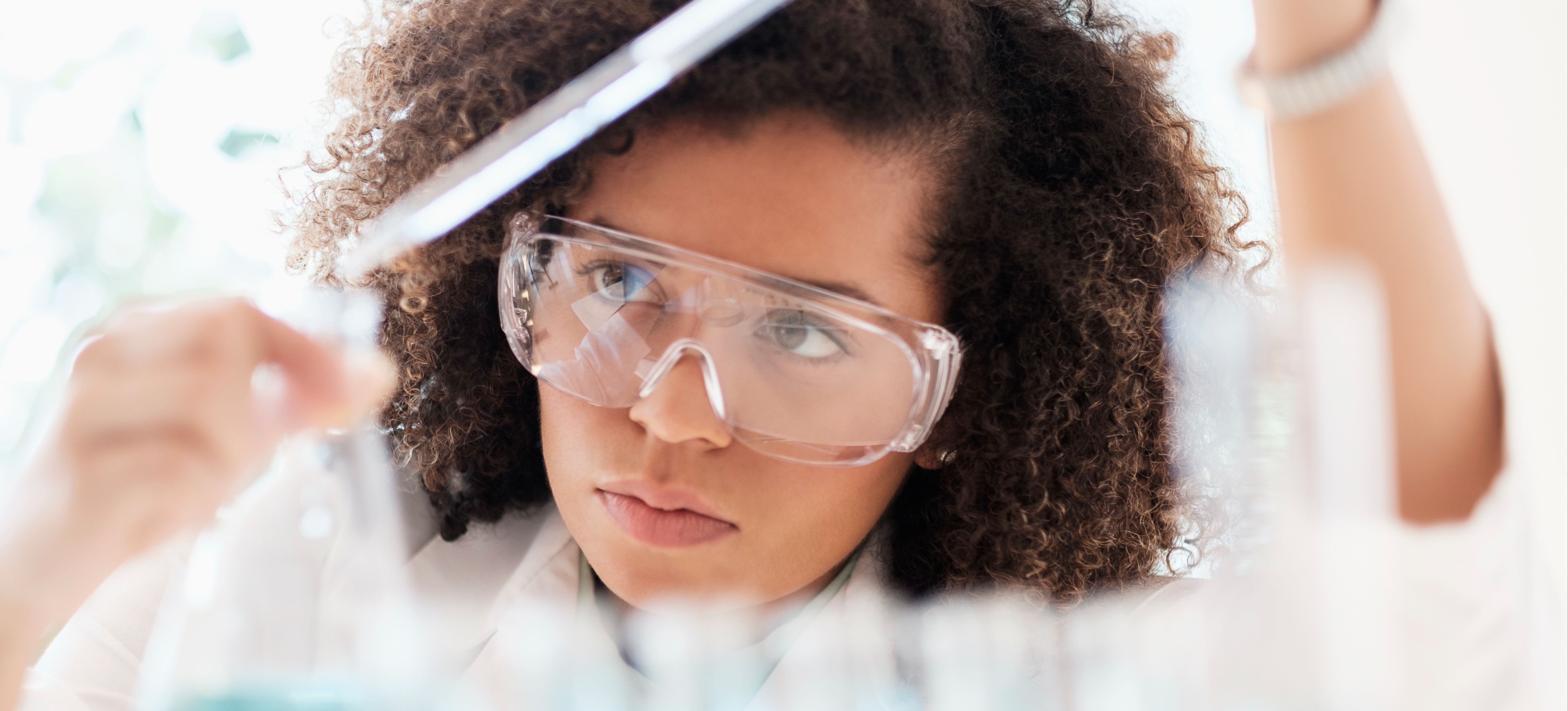 [Featured Image] A research scientist wearing protective goggles works with a pipette and test beakers.
