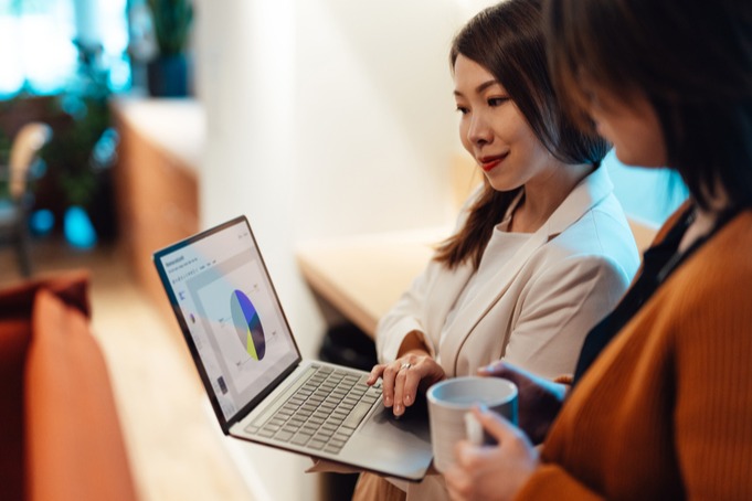 [Featured Image] Using skills learned from her business analyst certification, a businesswoman holding a laptop presents data to her colleague.
