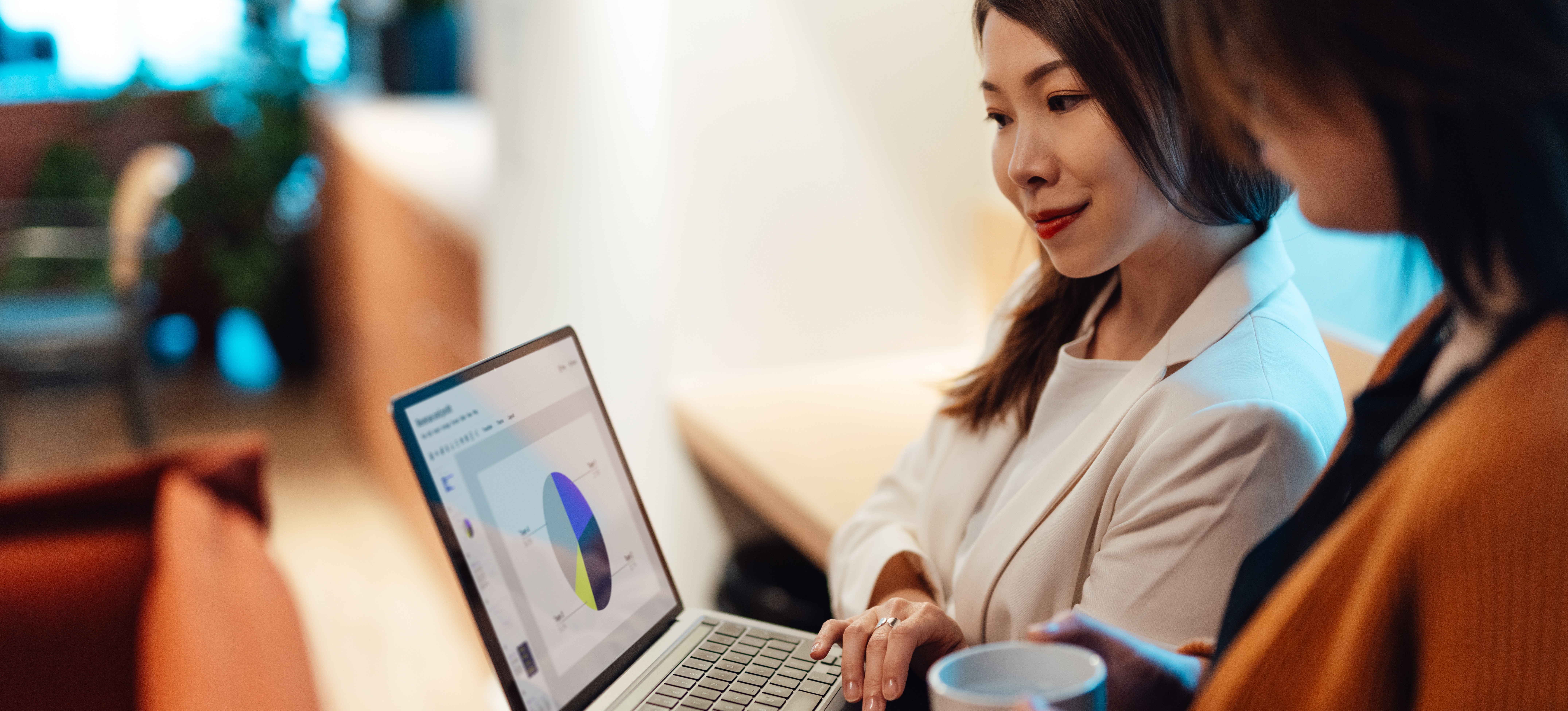 [Featured Image] Using skills learned from her business analyst certification, a businesswoman holding a laptop presents data to her colleague.
