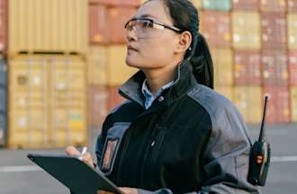 [Featured Image] A logistics specialist checks her tablet at a container terminal.