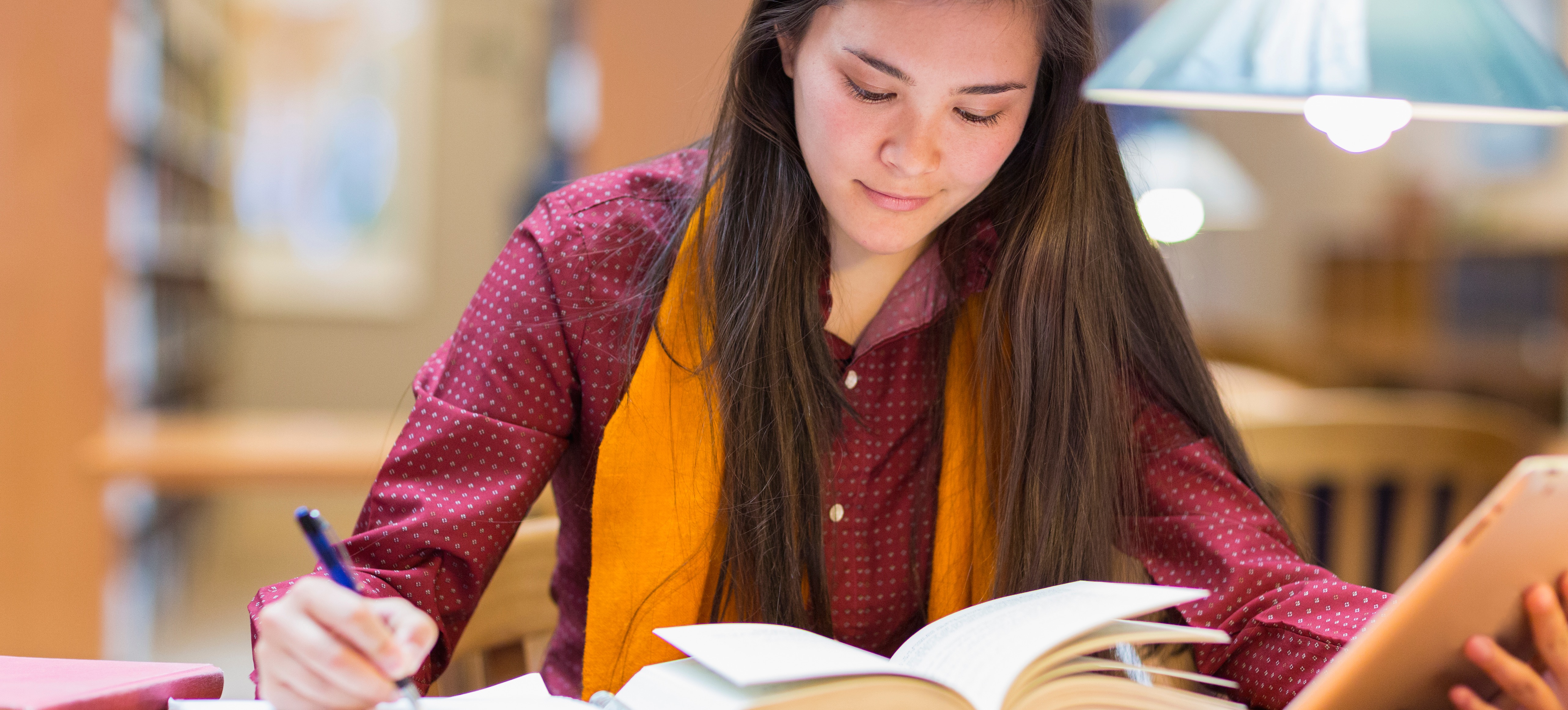 [Featured Image]: A student sits in a library, studying for a liberal arts degree.
