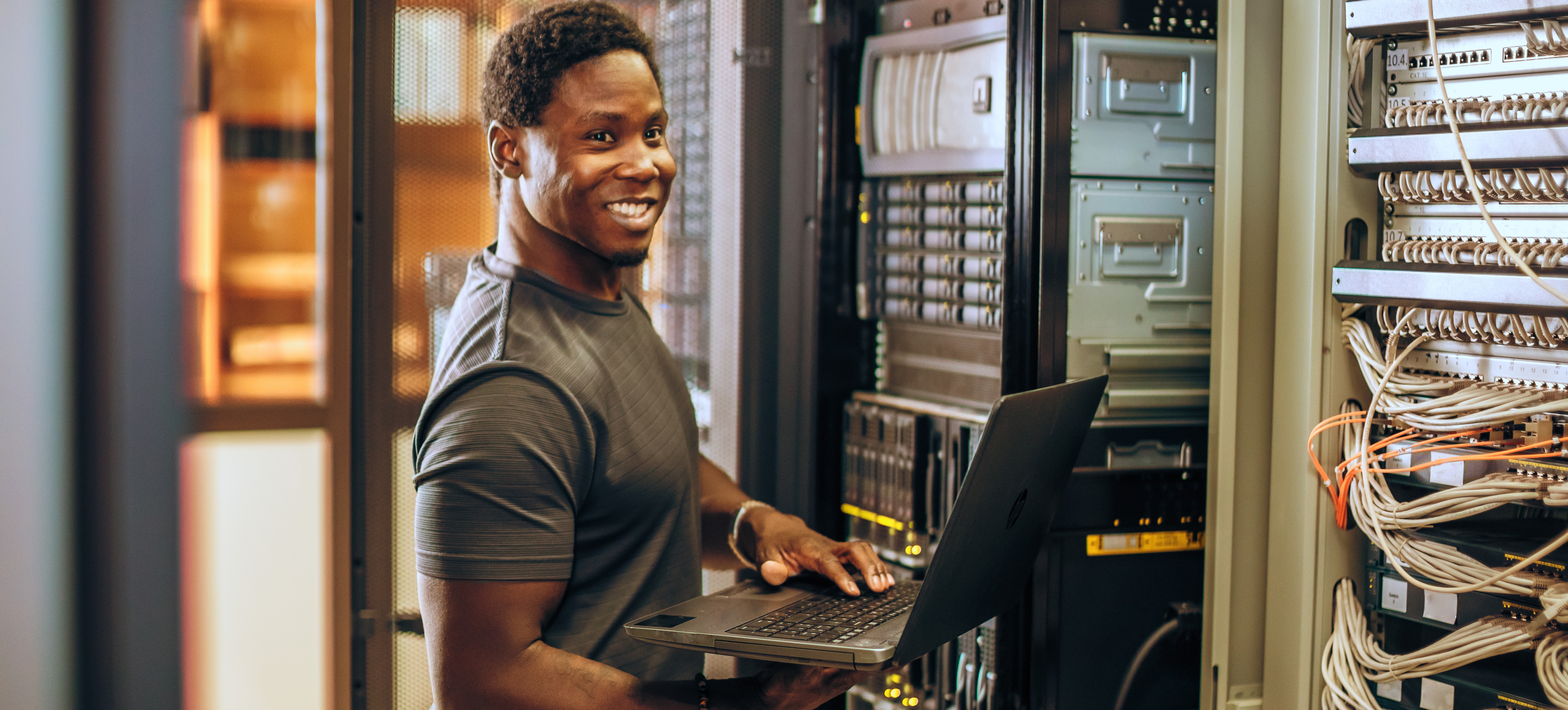 [Featured Image] A male networker is at a server holding a laptop working on his presentation layer found within the OSI model.
