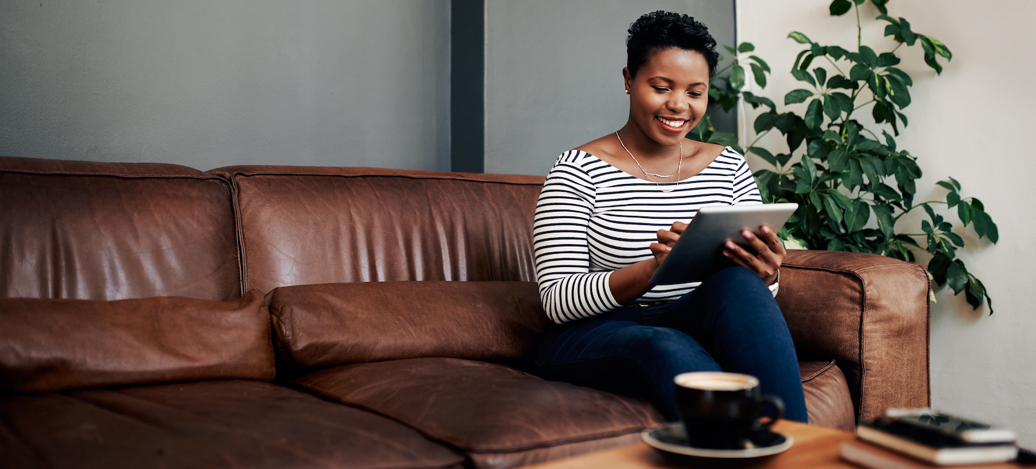 [Featured image] A person in a striped top sits on a leather couch and completes their FAFSA on a tablet. 