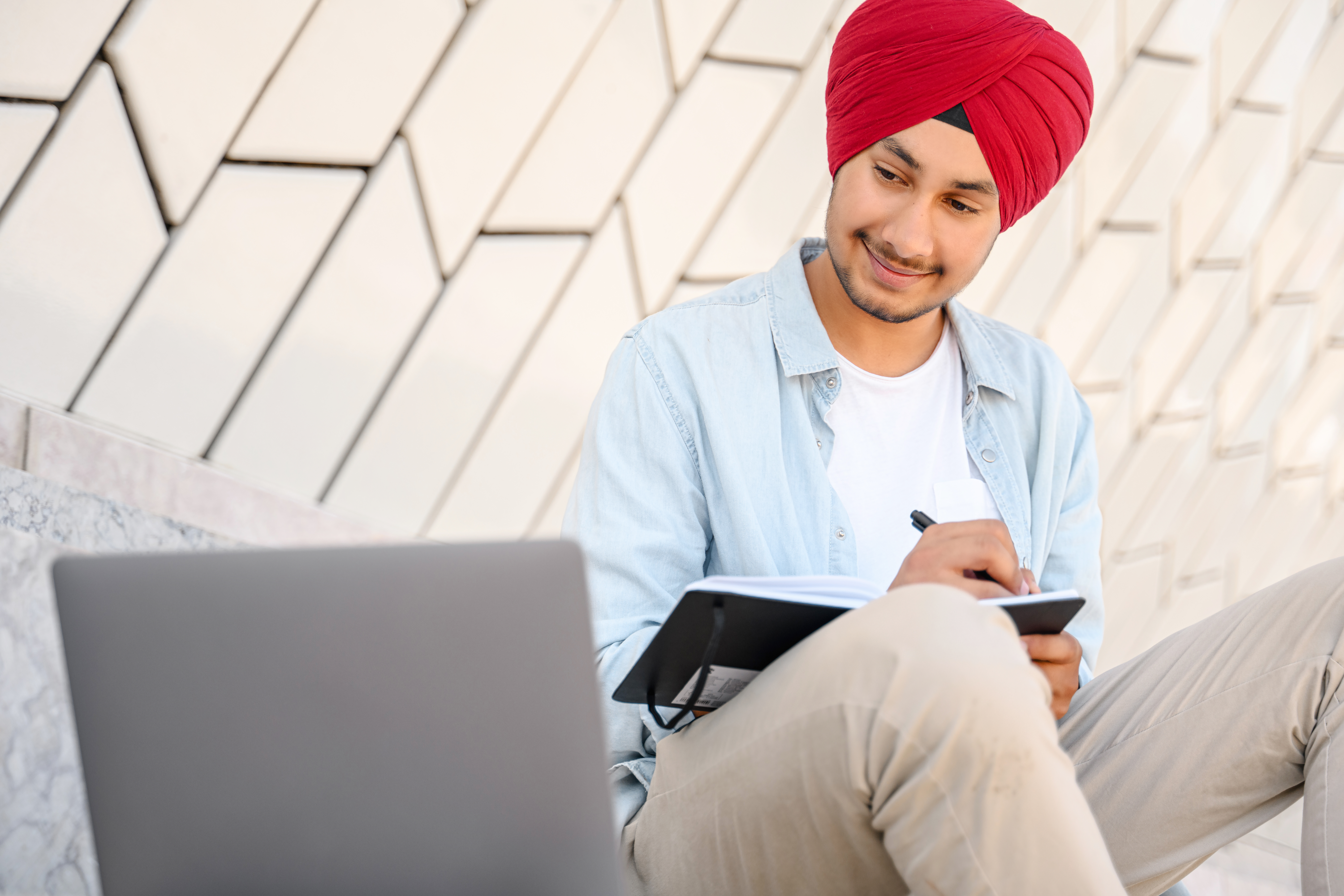 [Featured Image] A full-stack developer wearing a turban is looking at his computer and writing notes on paper when looking for jobs after BCA.