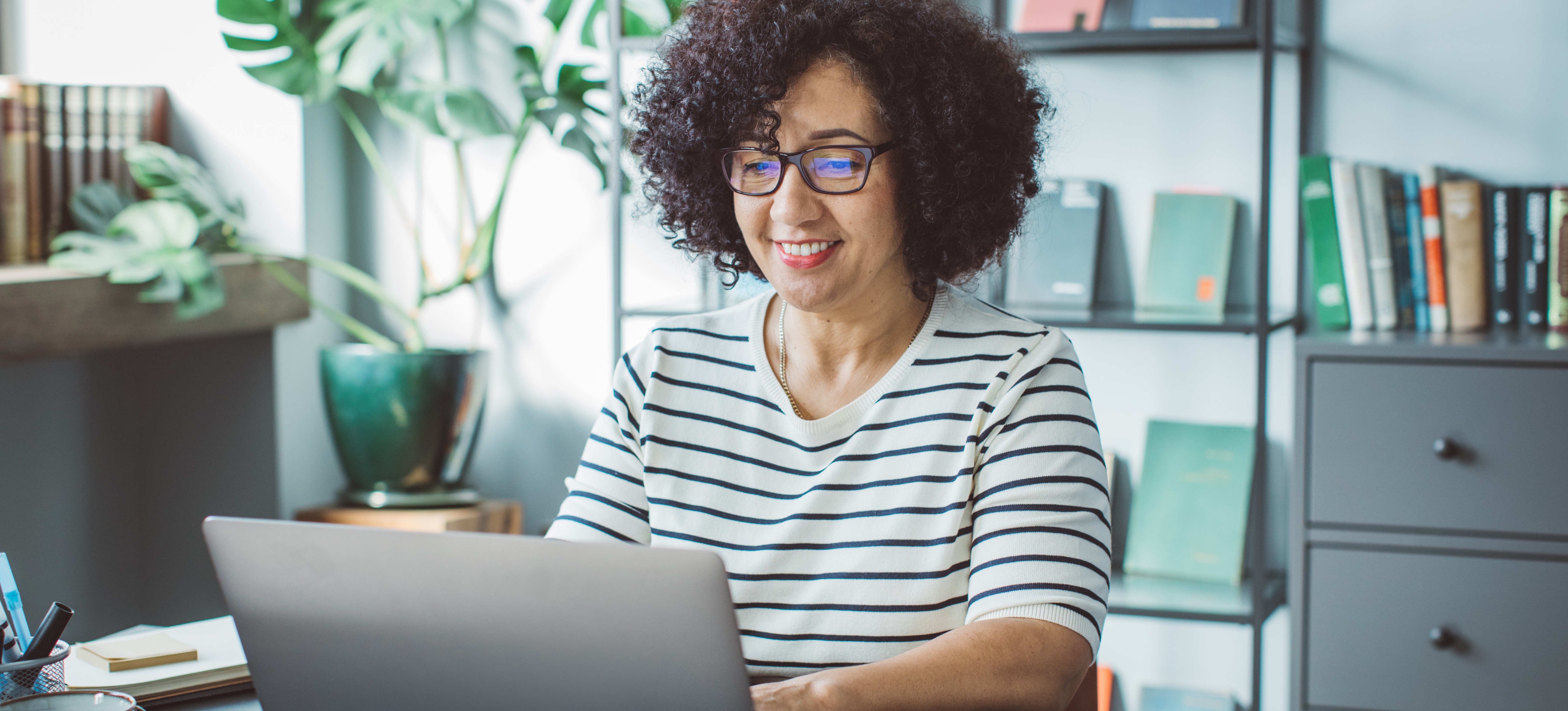 [FEATURED IMAGE] A smiling email marketing professional types on their laptop computer in an office.
