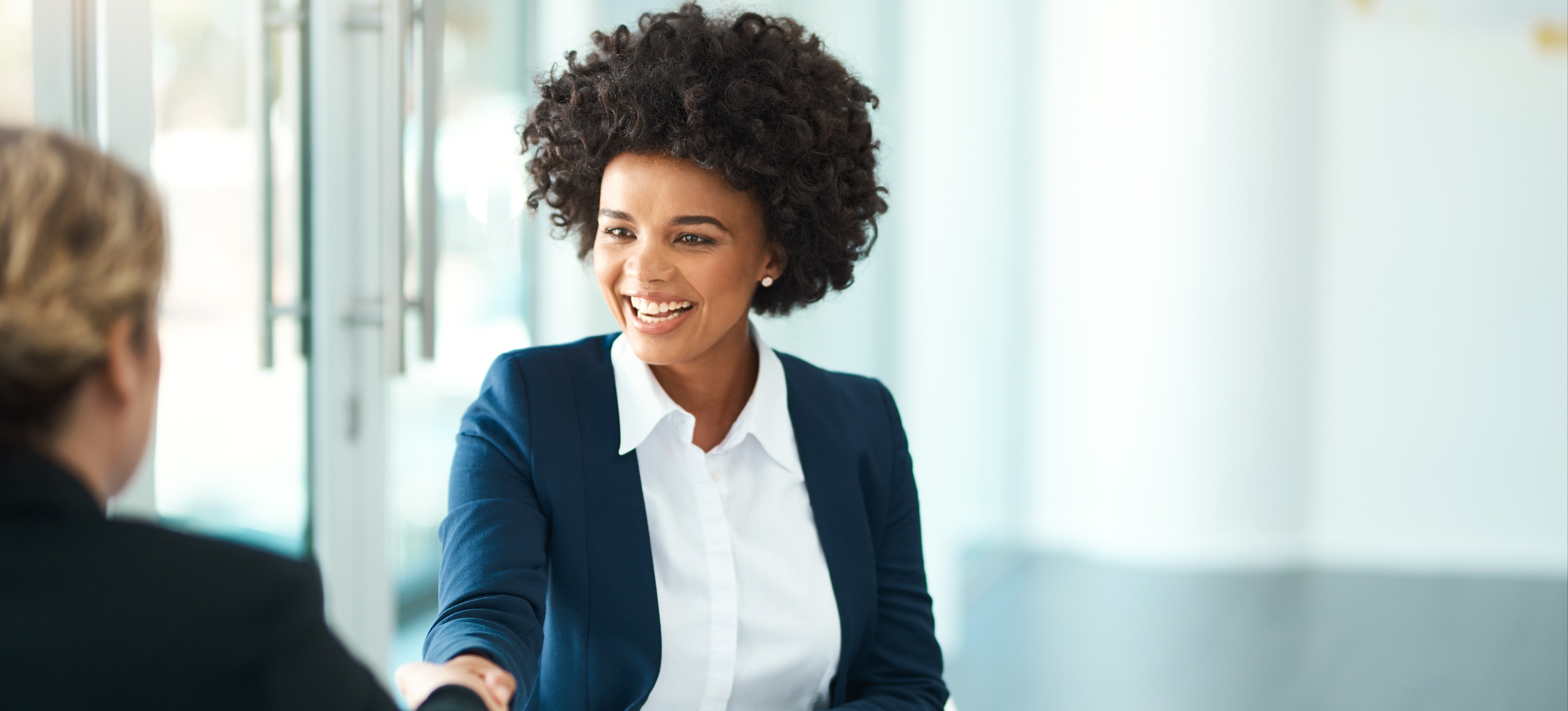 [Image en vedette] Une jeune femme, professionnelle de l'IA, assise à une table blanche dans un bureau, en train de passer un entretien avec des questions d'entretien sur le deep learning et de serrer la main de la personne qui l'interroge.
