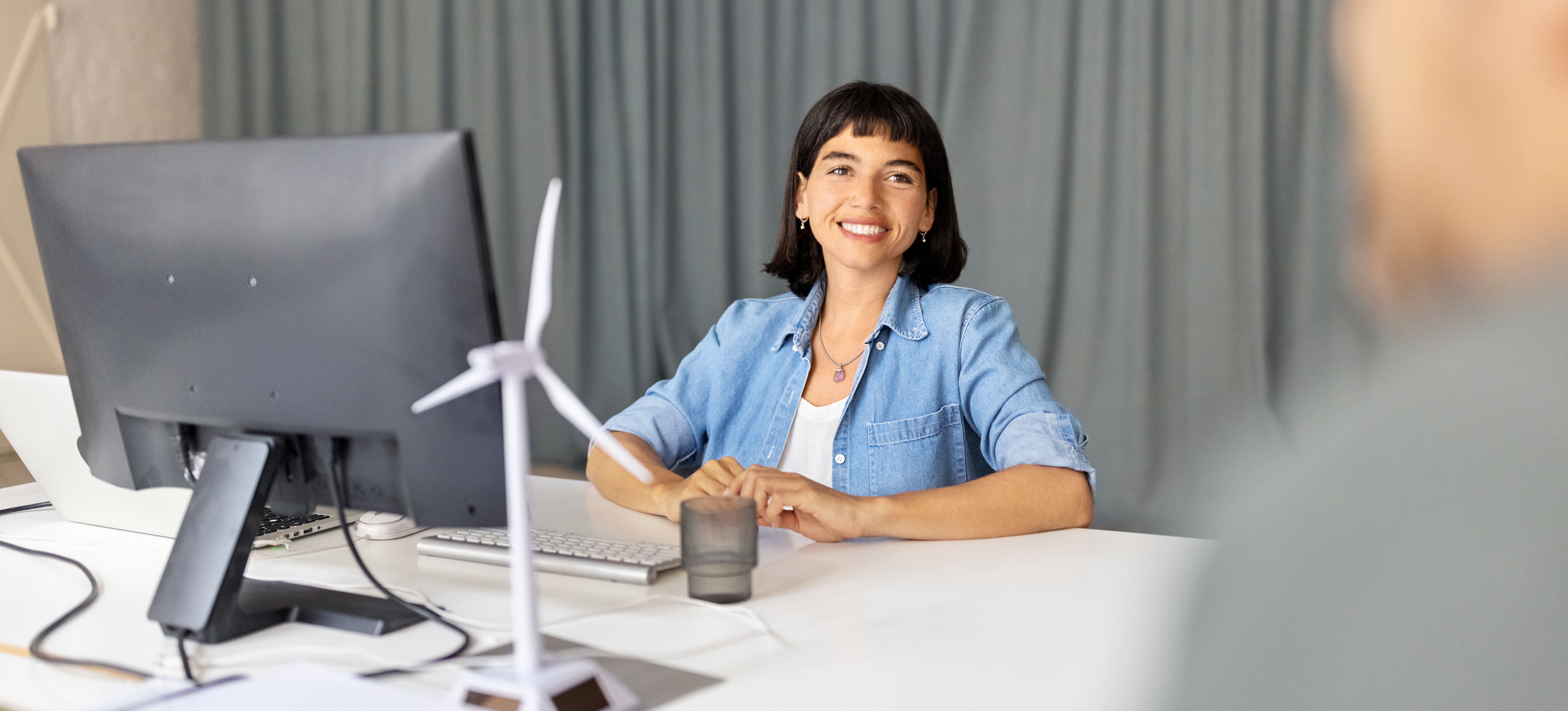 [Featured Image] A smiling automation engineer sits at their desktop computer and looks at a colleague off-camera.
