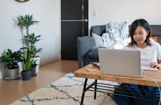 A woman sitting on the floor at her coffee table studying data analysis on her laptop