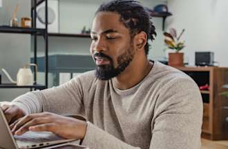 [Feature Image] A man sits at a laptop in his home and takes a Robotic Process Automation (RPA) exam prep course online. 
