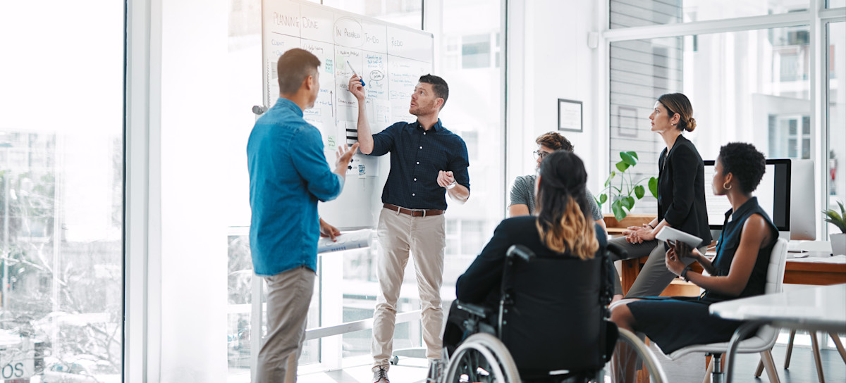 [Featured Image] A marketing team discusses their funnel marketing strategies, with one person pointing to a whiteboard while their colleagues watch.
