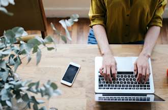 [Featured image] An SEO works on earning her Google Analytics Certification on a laptop computer. SHe has her phone and a red mug sitting on the table in front of her.