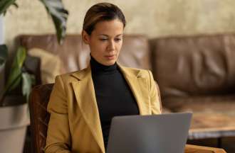 [Featured image] A person in a black turtleneck and yellow blazer sits at home working on their laptop.