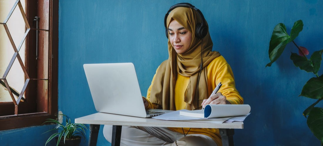 [Featured image] Person wearing yellow top and black headphones sits on the ground and converts Excel into Google Sheets in their laptop.