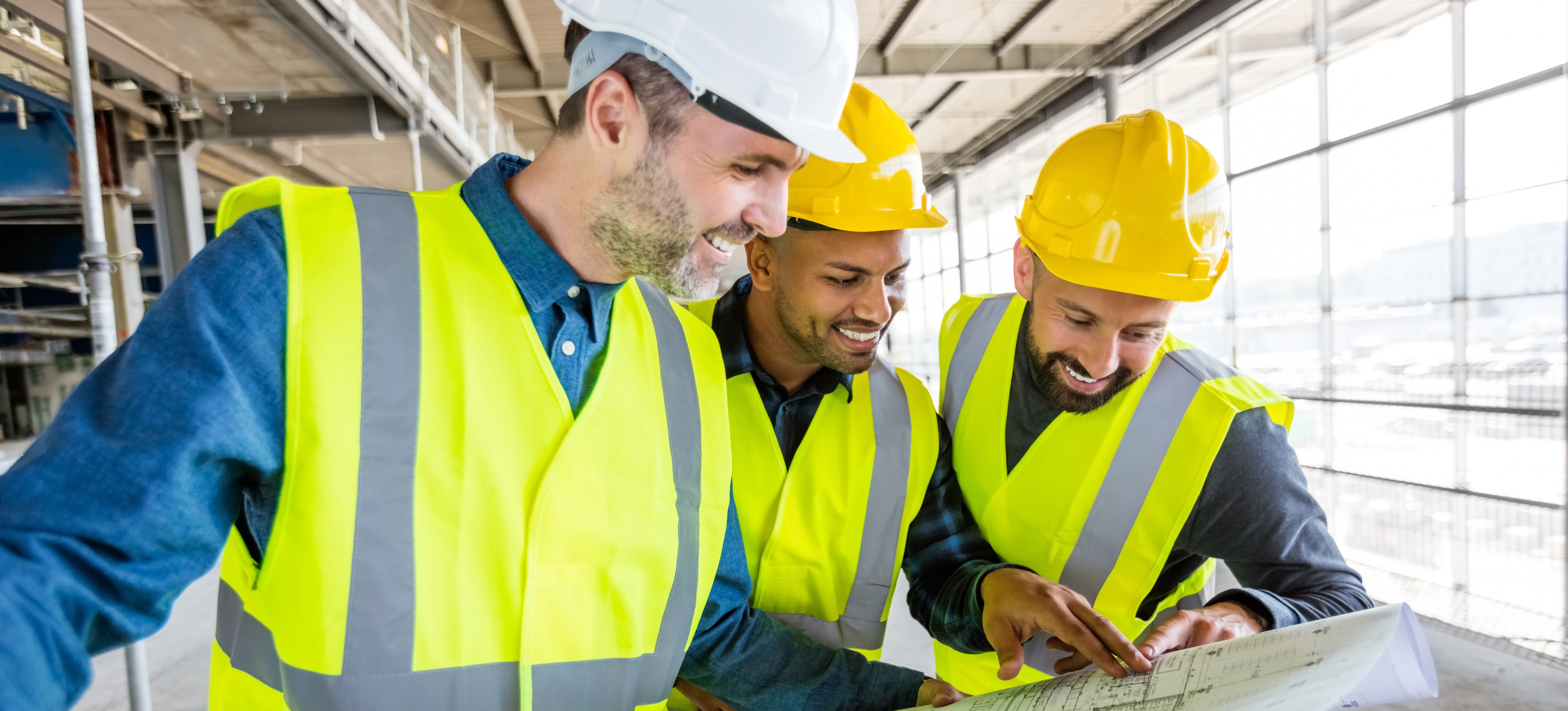 [Featured Image] A team of engineers at a construction site, analyzing blueprints and smiling while interacting about engineering certification.
