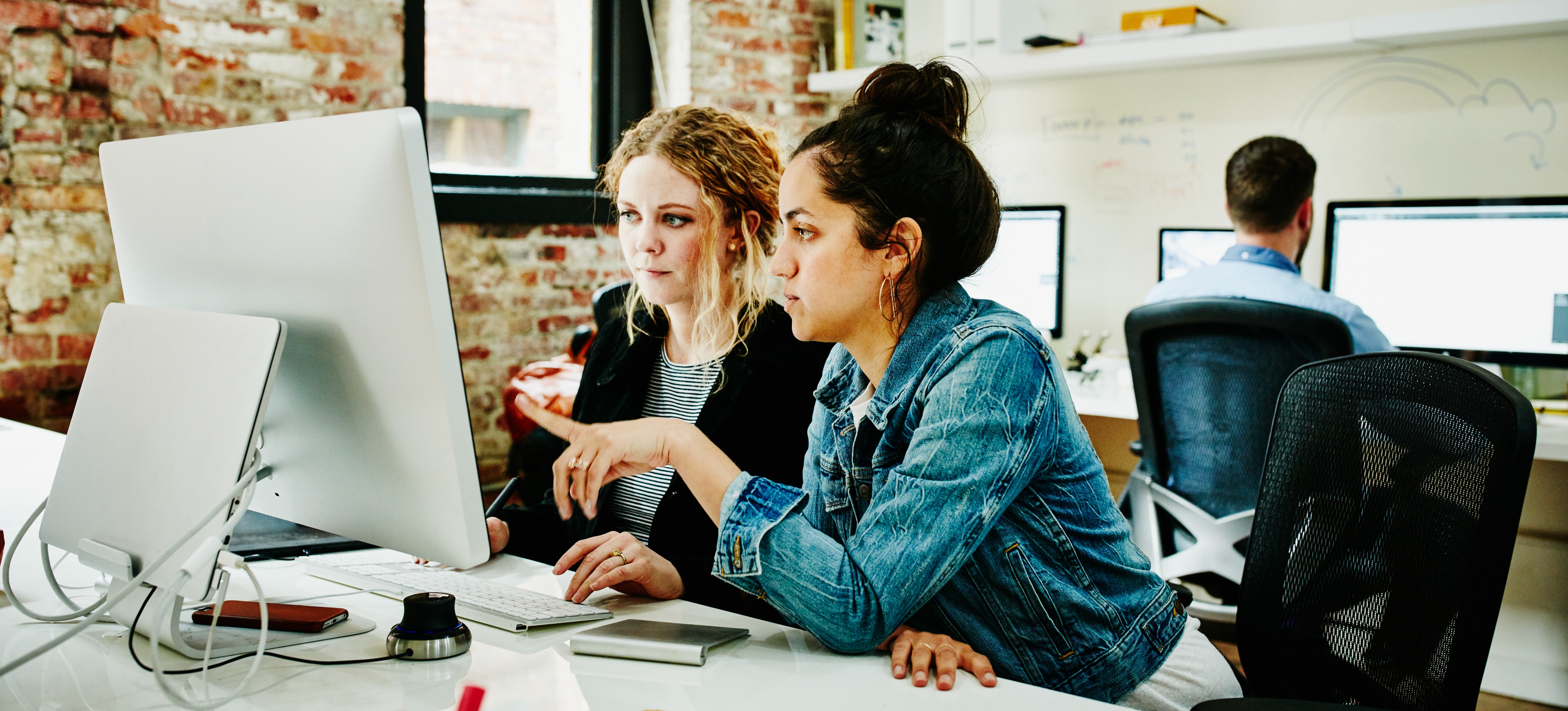[Featured Image] Two business professionals are looking at a computer monitor discussing a business process made easier through the use of an integrated software.
