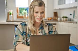 [Featured Image] A woman sits at her laptop in her kitchen and works on writing her Power BI resume. 
