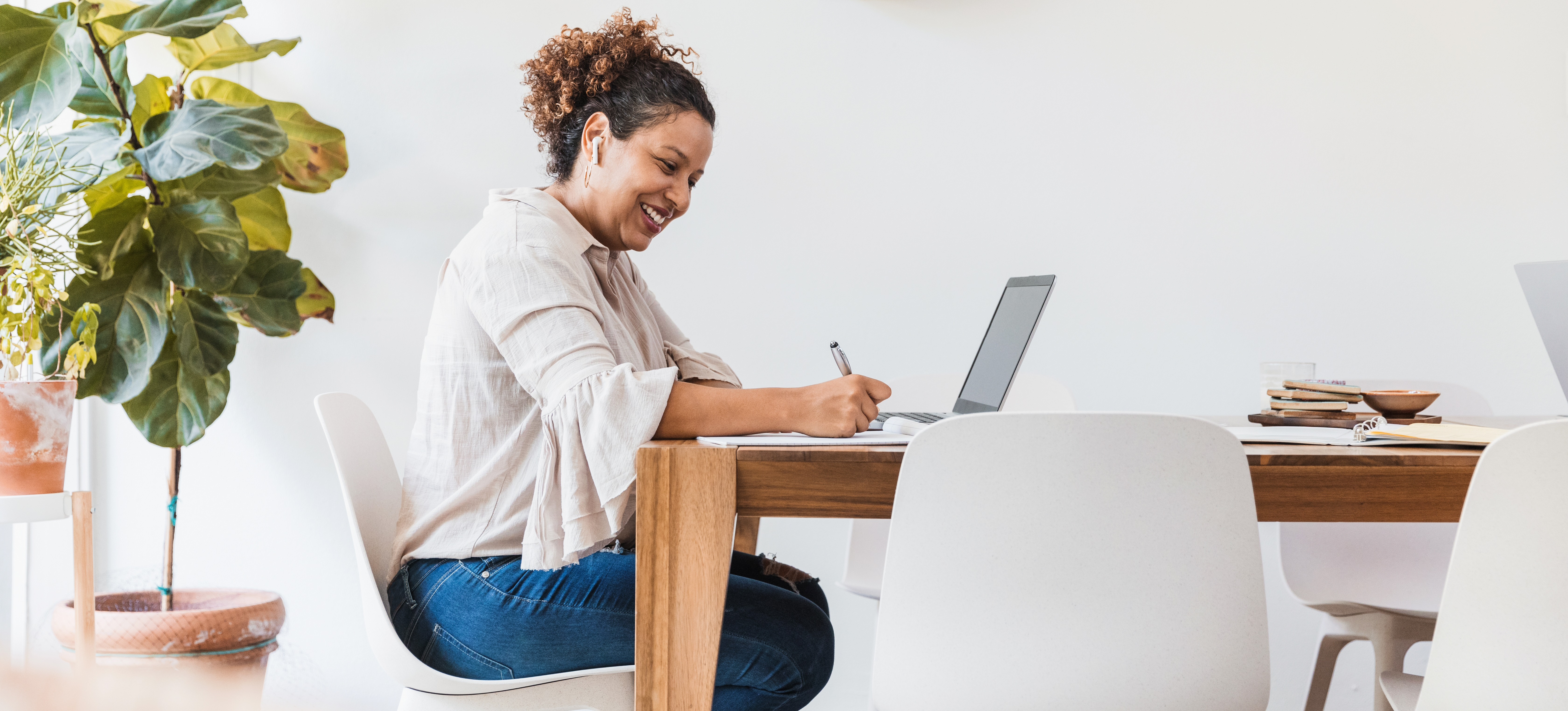 [Featured Image] A woman at home sits at her desk and uses a laptop and a notebook to research how to become a software engineer without a degree.
