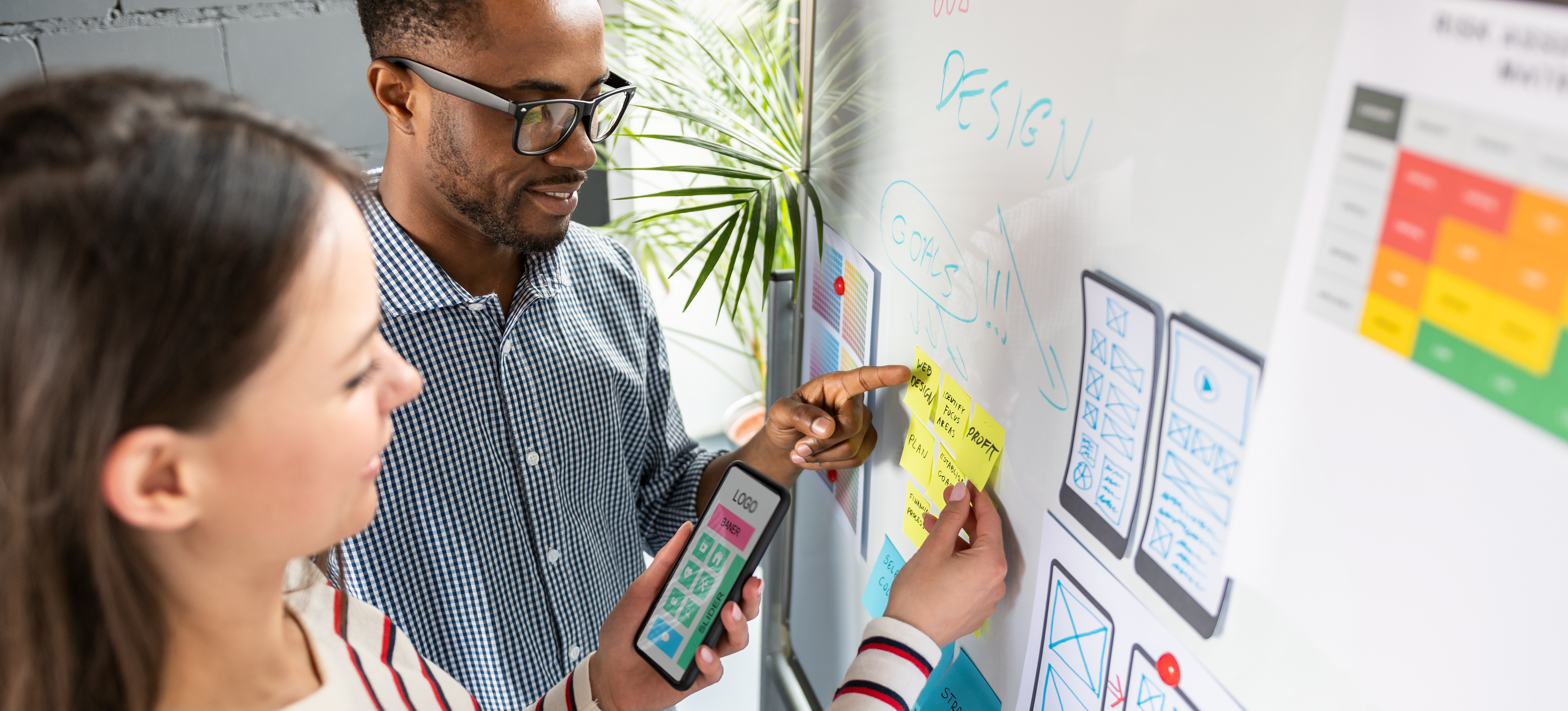 [Featured Image] Two co-workers map out a mobile app design on a whiteboard.