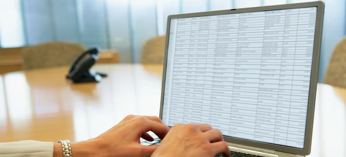 [Featured Image] The hands of a businessperson are typing on a laptop in a Google spreadsheet that has frozen rows of information.