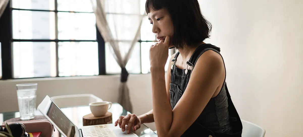 [Featured image] A professional following a UX designer career path works at a laptop computer.