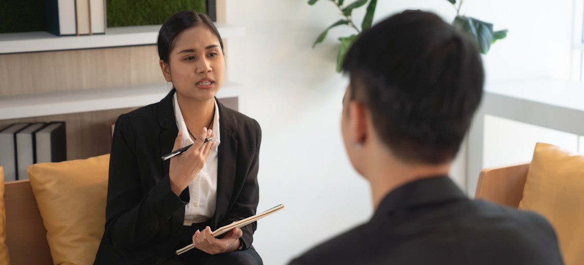 [Featured image] A hiring manager in a business suit writes on a notepad as they interview someone for a leadership role.
