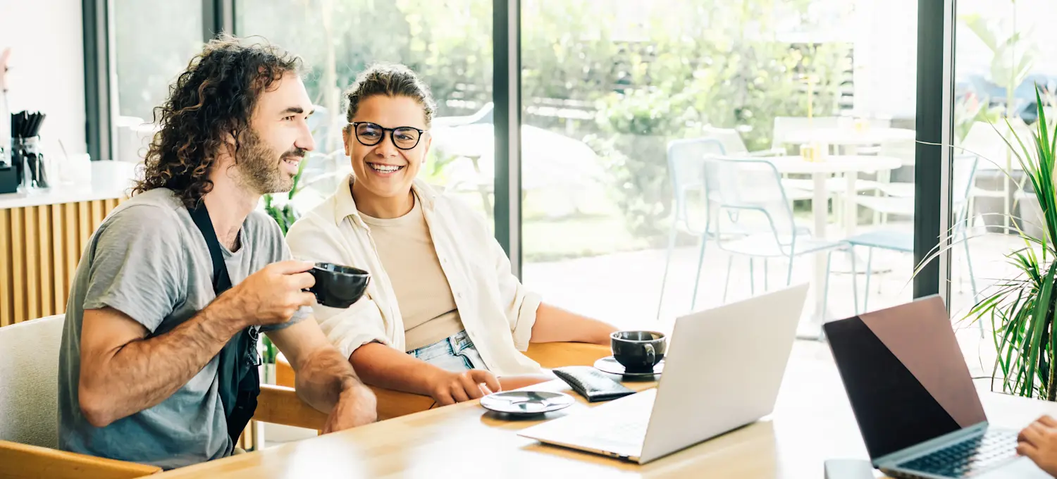 [Feature Image] Two cybersecurity professionals discuss the ISC2 certifications they are preparing for as they study in a brightly lit room and drink coffee.
