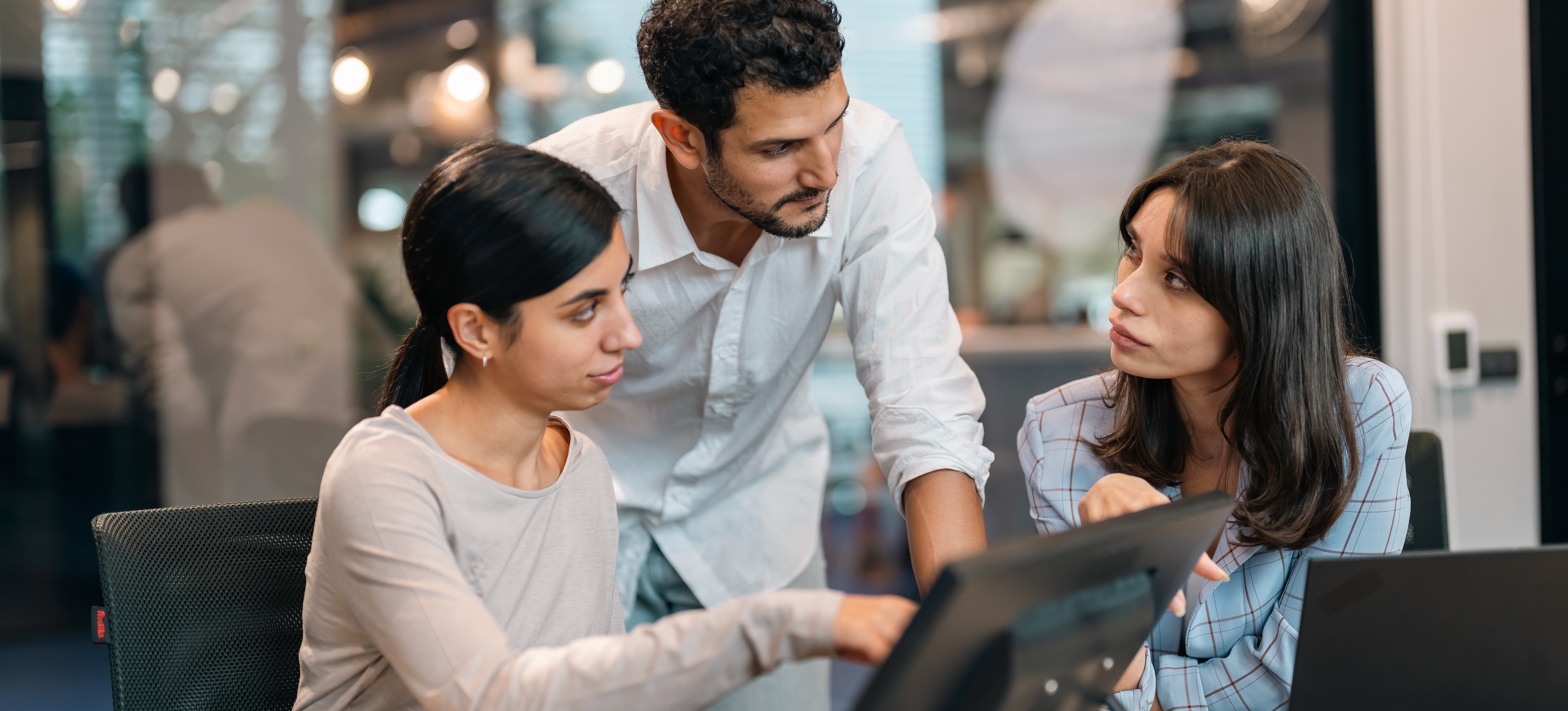 [Featured Image] Three colleagues sit in front of their laptops in an office setting and discuss cybersecurity best practices.