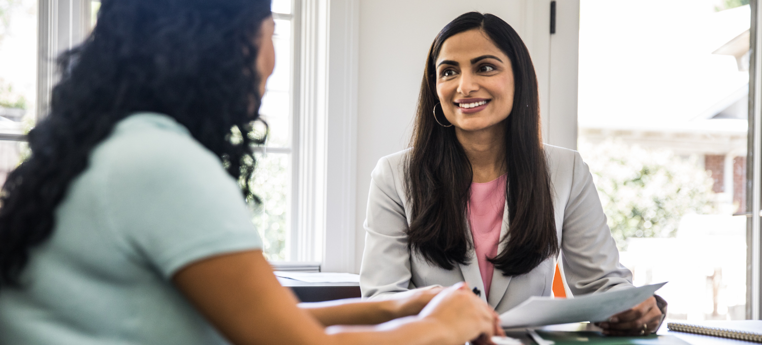 [Featured image] Two professionals sit at a conference table in professional dress, smiling at each other and discussing employability skills. 