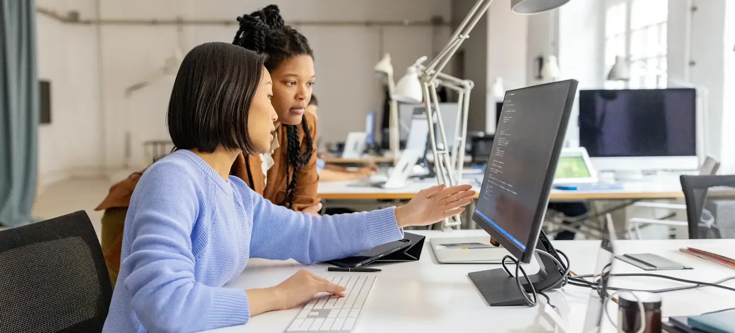 [Featured image] Two colleagues in a work setting discuss LangChain versus LangGraph as they look at a computer monitor.
