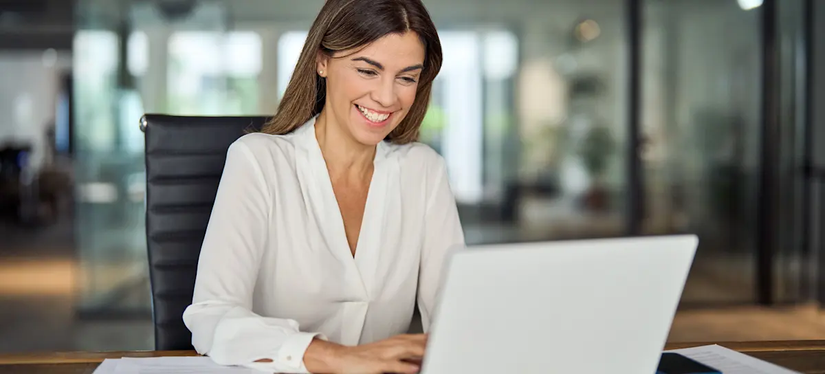 [Feature Image] A young businessperson working in a glass-walled office uses descriptive, predictive, and prescriptive analytics to drive informed decisions. 
