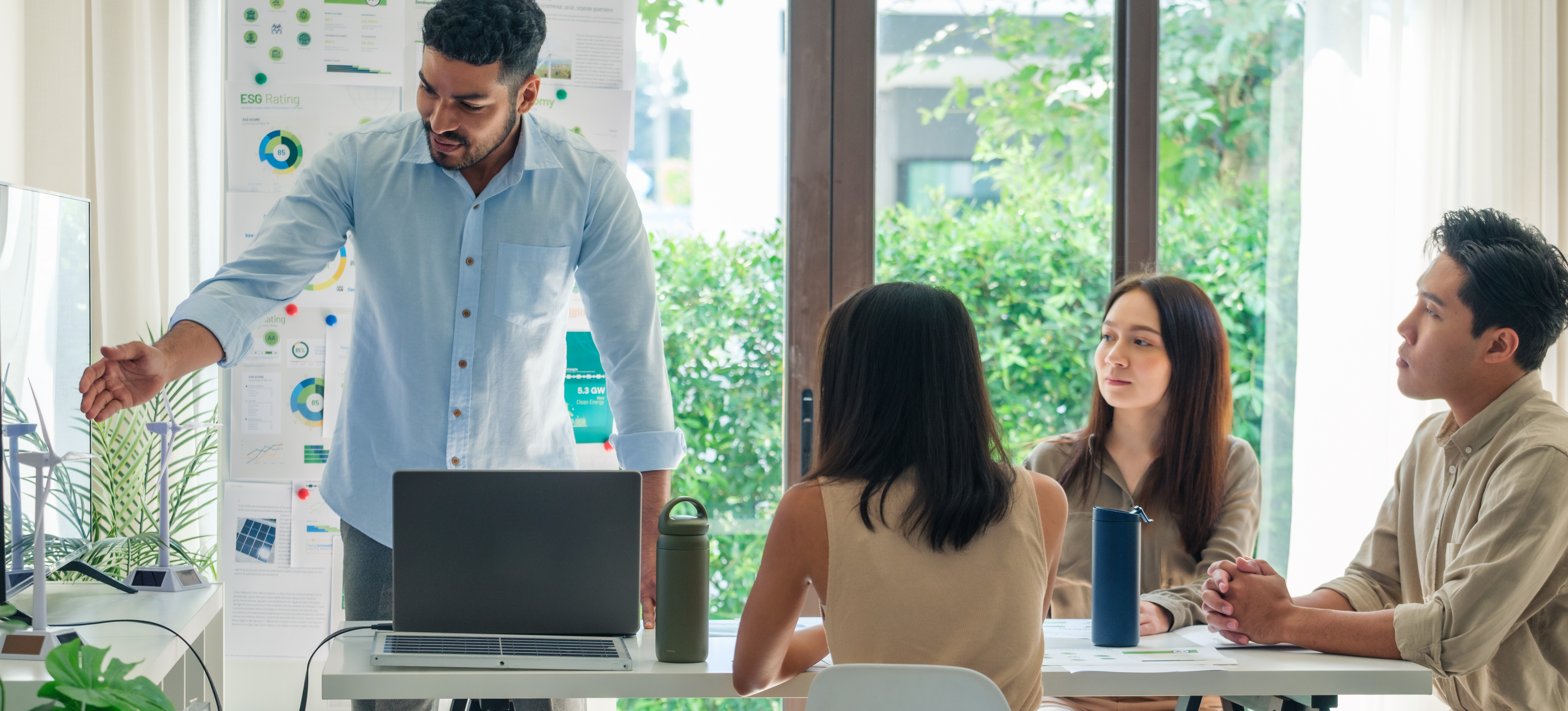 [Featured Image] Four coworkers discuss design management in a sunny conference room.