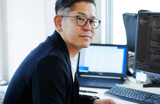 [Featured image] A machine learning engineer sits at his workstation with a laptop and a monitor.