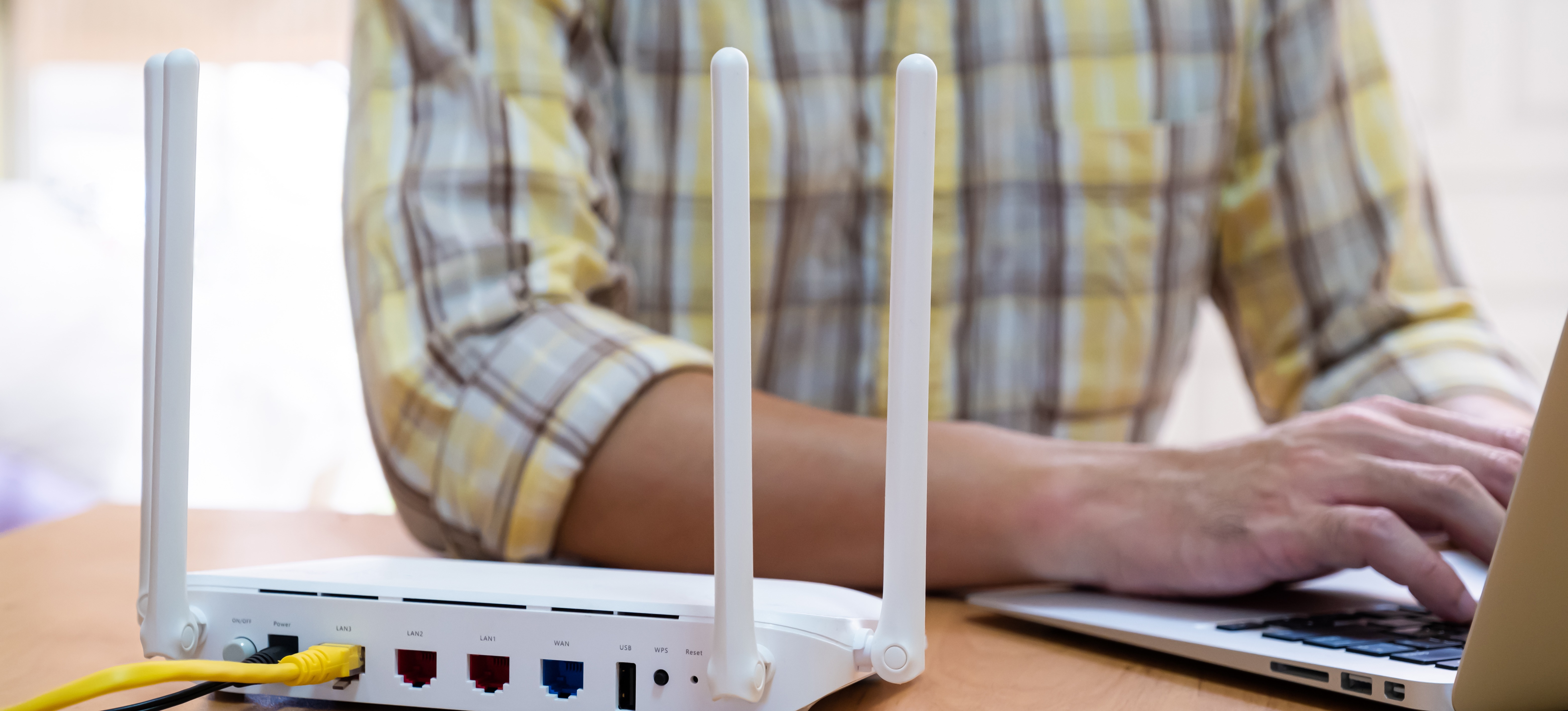 [Featured Image] A person in a yellow plaid shirt works on their computer after determining the proper network topology for their needs. 
