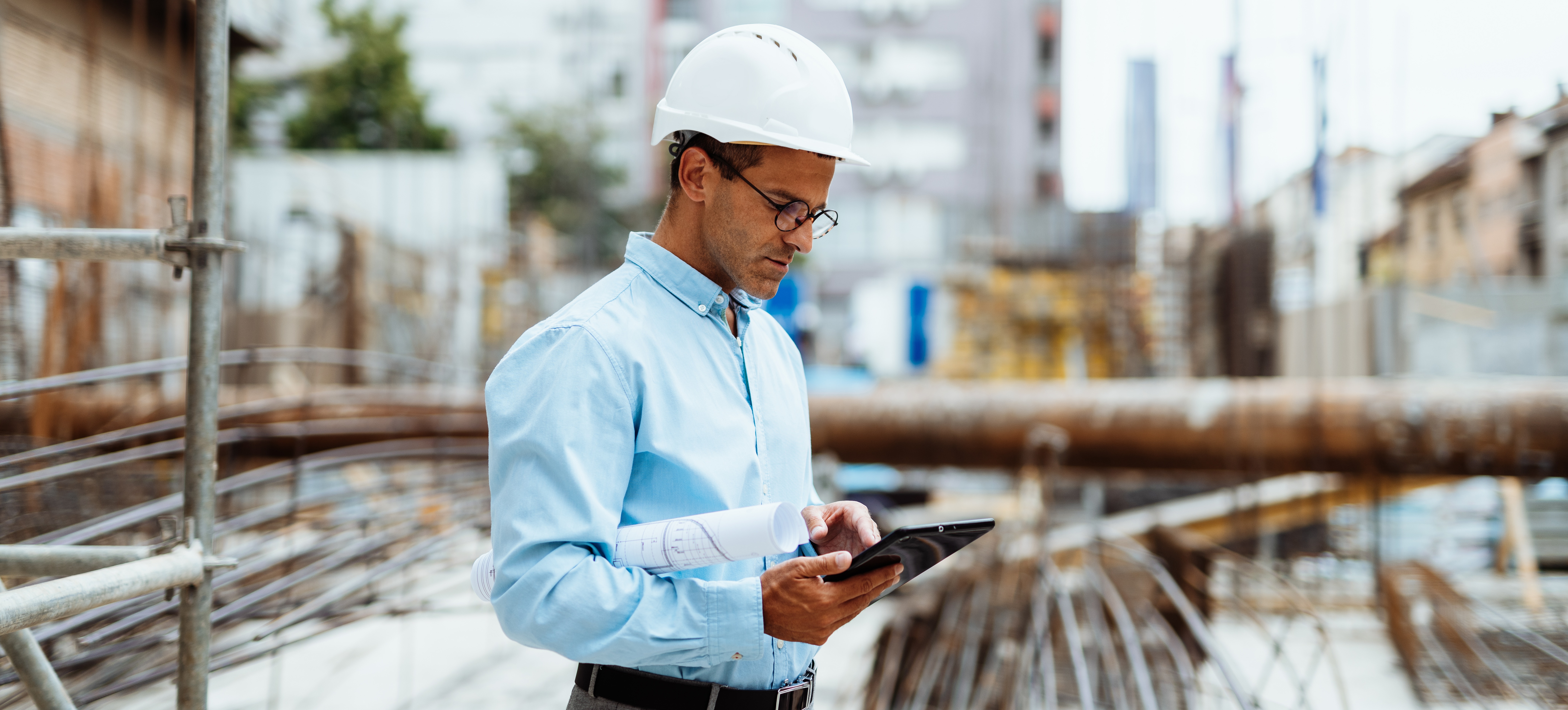[Featured Image] A manager with an engineering management degree evaluates engineering blueprints at a job site. 
